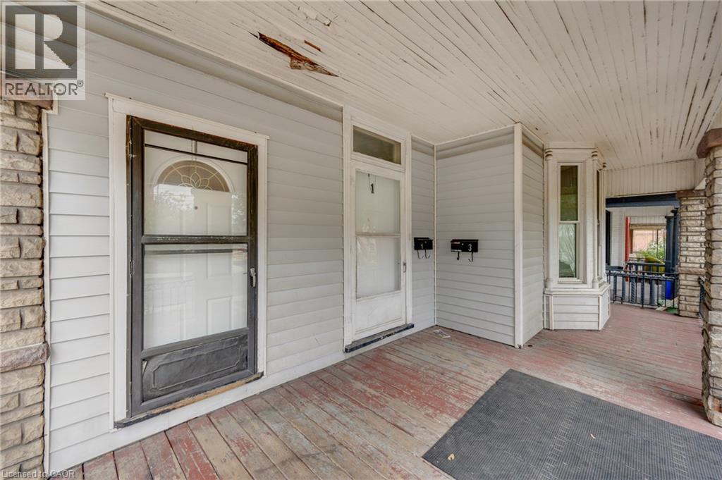Front porch featuring weathered wood flooring, stone-clad columns, horizontal siding, and multiple entry points - 211 Wentworth Street N, Hamilton, ON