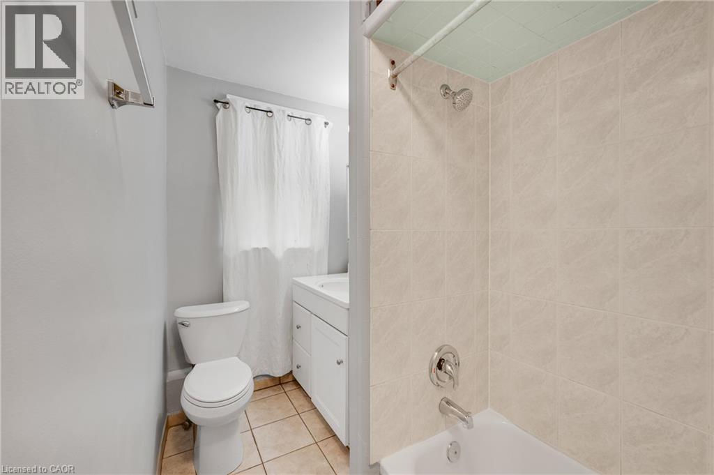 Bathroom featuring a tiled shower surround, integrated bathtub, white vanity with cabinet storage, and tile flooring - 211 Wentworth Street N, Hamilton, ON