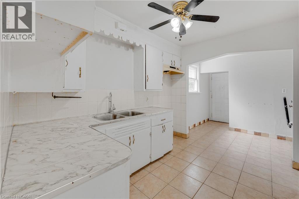 White cabinetry with brass hardware, dual basin stainless steel sink, patterned countertop, ceramic tile backsplash, and ceramic tile flooring - 211 Wentworth Street N, Hamilton, ON