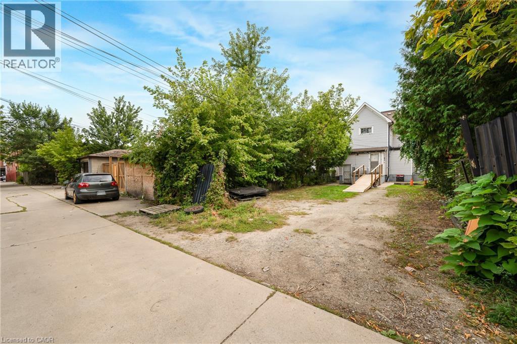 Gravel driveway with a wooden ramp entrance, featuring mature perimeter trees and a concrete pathway - 211 Wentworth Street N, Hamilton, ON
