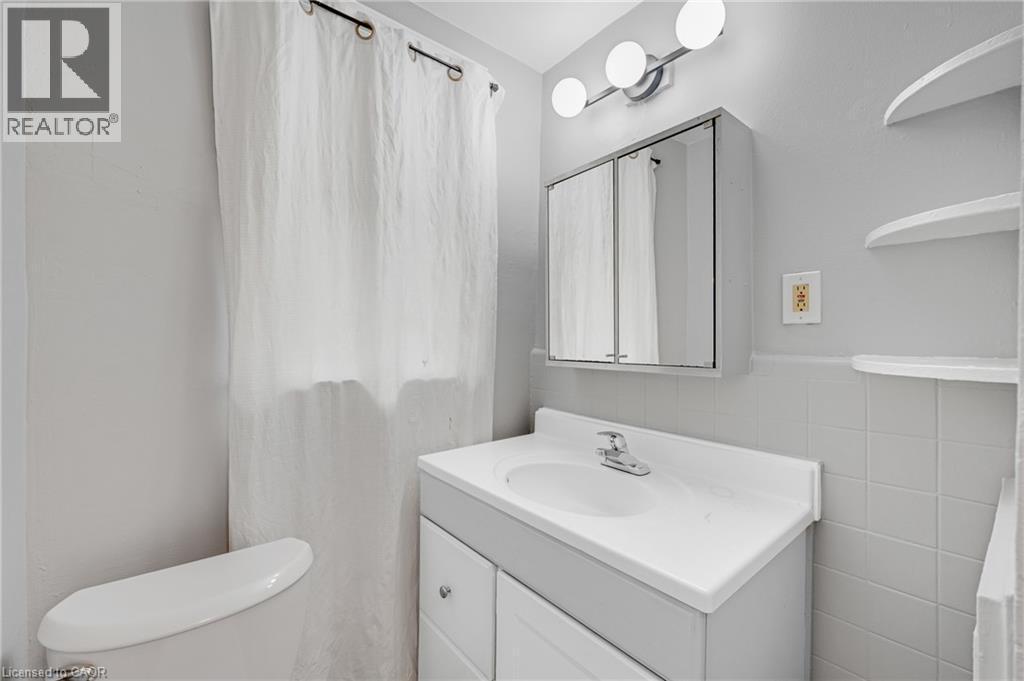 Vanity with an integrated sink and chrome faucet, medicine cabinet with mirrored doors, and wall-mounted spherical light fixture - 211 Wentworth Street N, Hamilton, ON