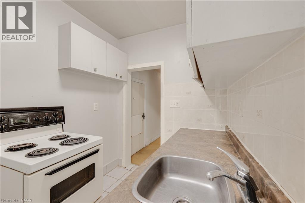 Kitchen featuring a white electric range, stainless steel sink, tiled backsplash, and white cabinetry - 211 Wentworth Street N, Hamilton, ON