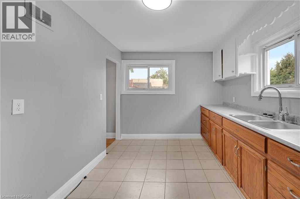Kitchen featuring wood cabinetry, a dual basin stainless steel sink, a modern pull-down faucet, and tile flooring - 211 Wentworth Street N, Hamilton, ON