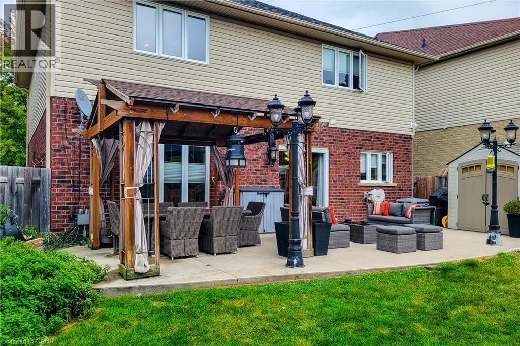 Expansive concrete patio featuring a wood pergola, brick exterior, and manicured lawn - 214 Cloverleaf Drive, Ancaster, ON