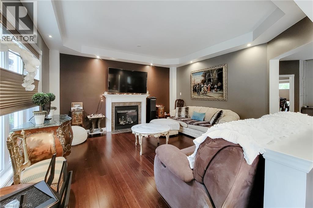 Hardwood flooring, tray ceiling with recessed lighting, integrated fireplace, and a large window with privacy blinds - 214 Cloverleaf Drive, Ancaster, ON