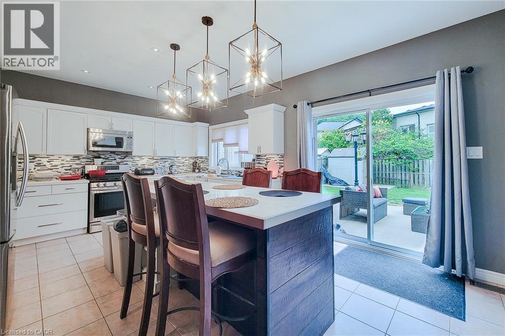 Kitchen featuring white cabinetry, tile flooring, stainless steel appliances, and a central island with a light-toned countertop - 214 Cloverleaf Drive, Ancaster, ON