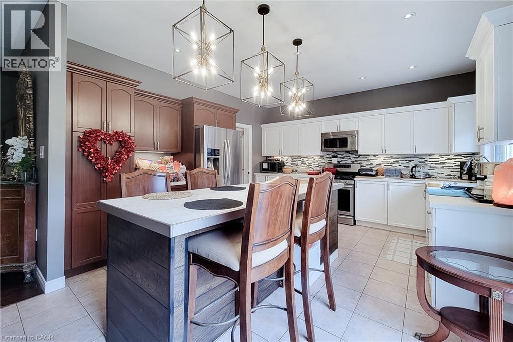 Kitchen featuring a multi-tone cabinetry design, central island with a light-toned countertop, stainless steel appliances, and a mosaic tile backsplash - 214 Cloverleaf Drive, Ancaster, ON