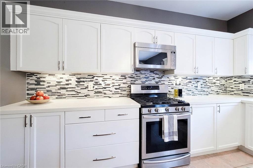 White cabinetry, stainless steel range and microwave, light-toned countertops, and a mosaic tile backsplash - 214 Cloverleaf Drive, Ancaster, ON