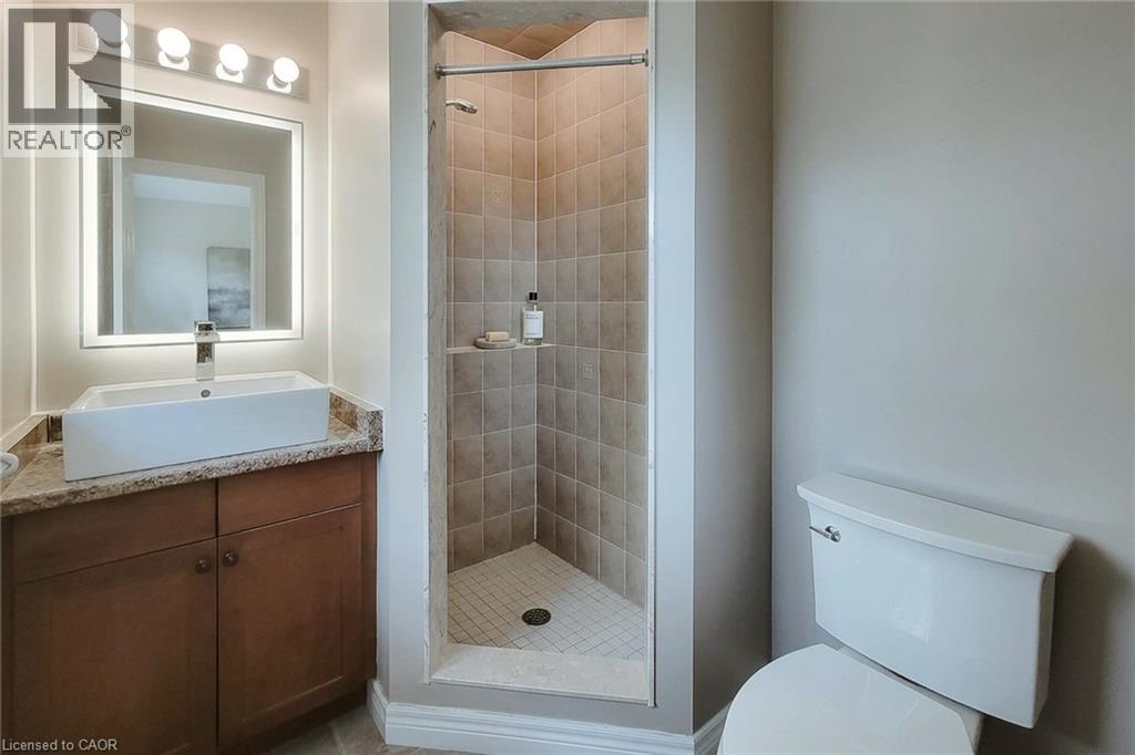 Vanity with a vessel sink, integrated lighting in the mirror, wood-finish cabinetry, and a tiled shower with a glass enclosure - 214 Cloverleaf Drive, Ancaster, ON