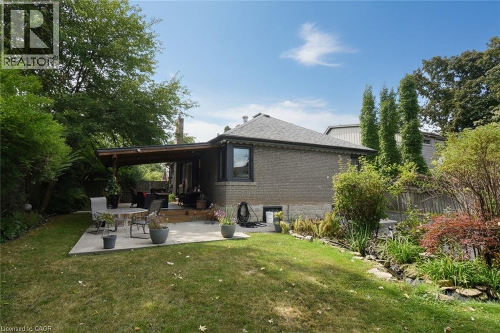 Expansive backyard featuring a manicured lawn, concrete patio, and a covered wooden deck - 154 Ewen Road, Hamilton, ON