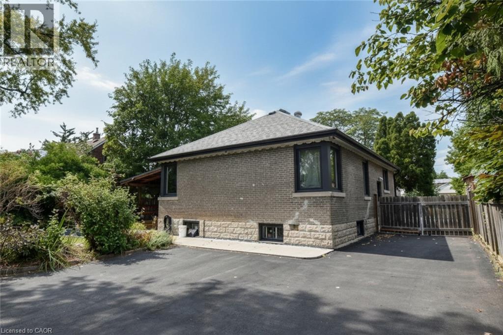 Brick exterior with stone foundation detailing, bay window, dark window trim, and a shingle roof - 154 Ewen Road, Hamilton, ON