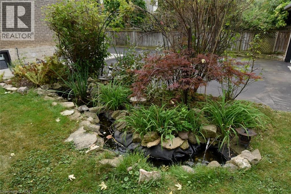 Water feature with rock border, surrounded by mature plantings and a manicured lawn - 154 Ewen Road, Hamilton, ON