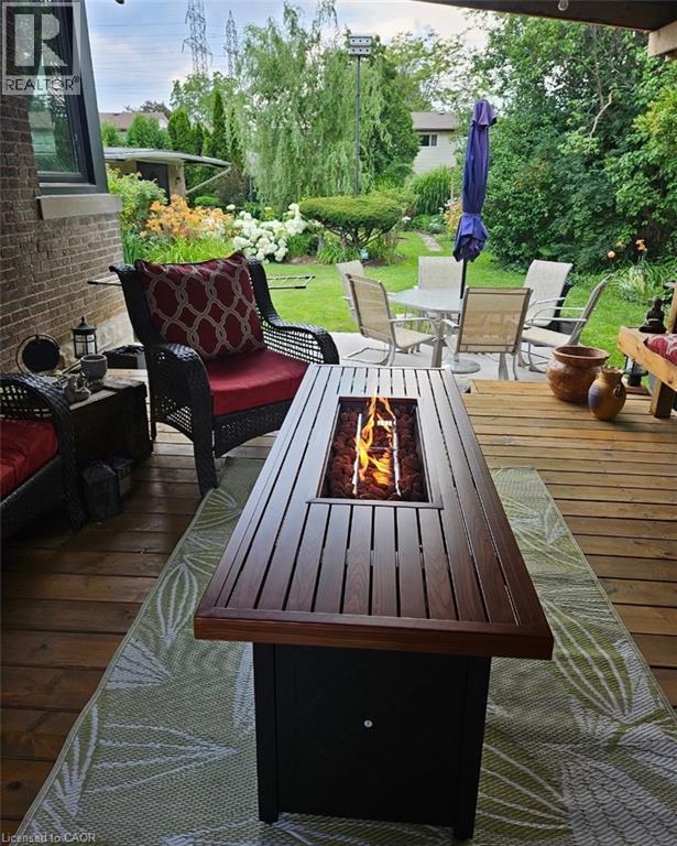 Expansive wooden deck with a built-in fire feature, overlooking a landscaped backyard with mature greenery and a stone patio - 154 Ewen Road, Hamilton, ON