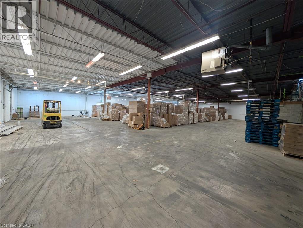 Expansive concrete flooring in a large open warehouse space with exposed structural beams and overhead fluorescent lighting - 97 Ardelt Avenue, Kitchener, ON