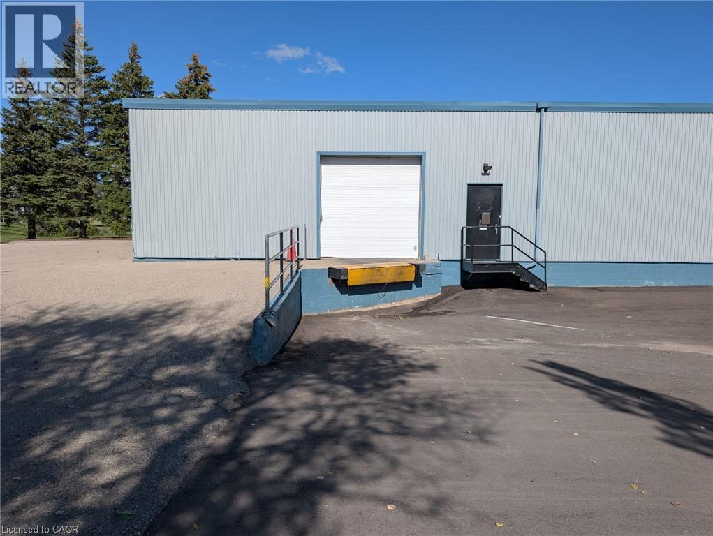 Corrugated metal siding with a blue trim, a white roll-up door, an exterior entrance with black stairs and handrails, and an asphalt parking area - 97 Ardelt Avenue, Kitchener, ON