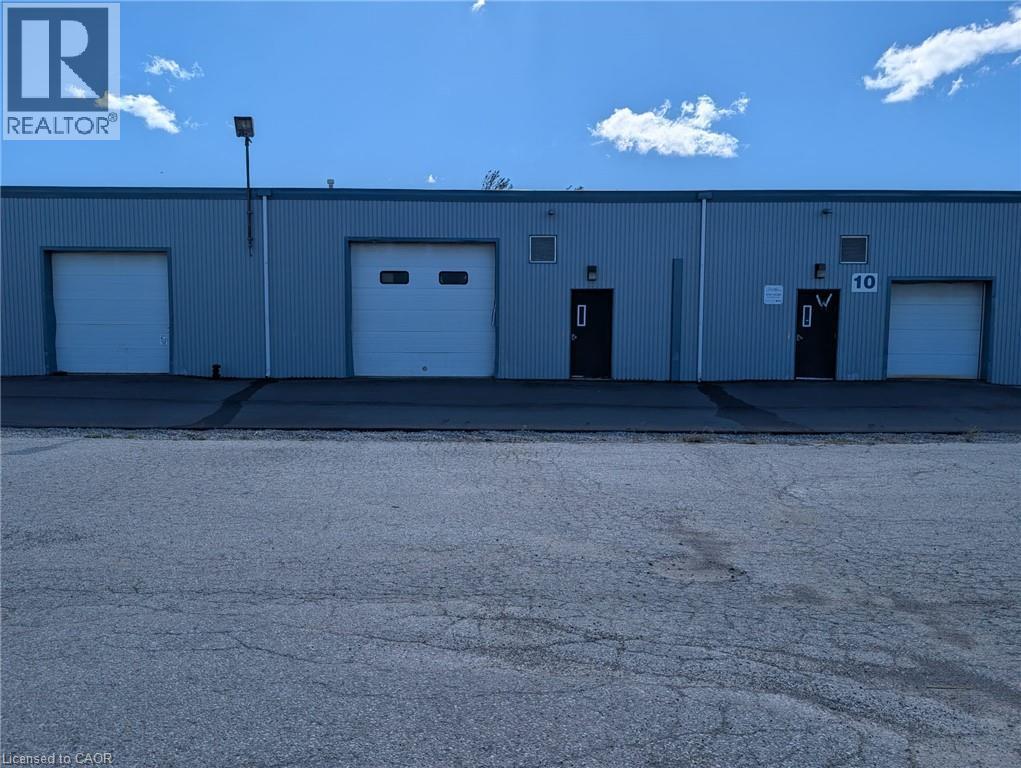Corrugated metal exterior with multiple roll-up doors, ground-level entry doors, and exterior lighting fixtures - 97 Ardelt Avenue, Kitchener, ON