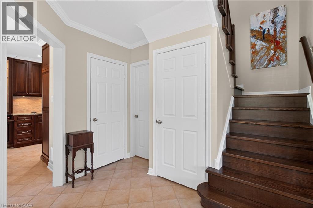 Entryway featuring wood-finish staircase, crown molding, paneled doors, and square tile flooring - 1347 Brookstar Drive, Oakville, ON