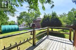 Expansive outdoor deck with wood railing, overlooking a large grassy area and mature trees -