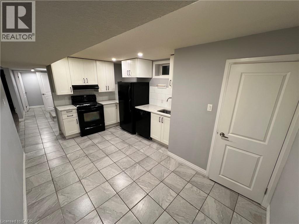 Kitchen featuring white cabinetry, light-toned countertops, tile flooring, and integrated black appliances - 33 Ruskview Road Unit# Lower, Kitchener, ON
