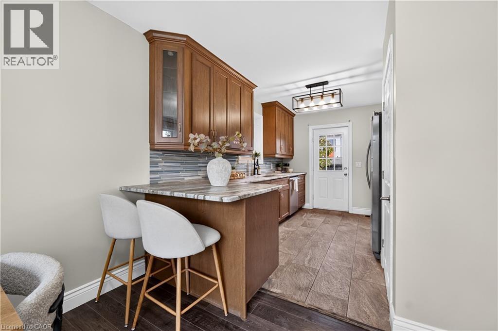 Wood-finish cabinetry with glass accents, stone-look countertop, rectangular tile backsplash, and a modern ceiling fixture - 176 Avalon Place, Kitchener, ON