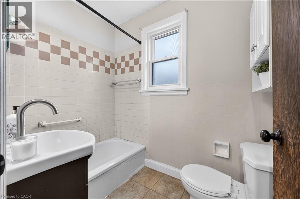 Bathroom featuring tiled walls with decorative accents, an integrated bathtub and shower, a window with white trim, and a wall-mounted medicine cabinet - 176 Avalon Place, Kitchener, ON