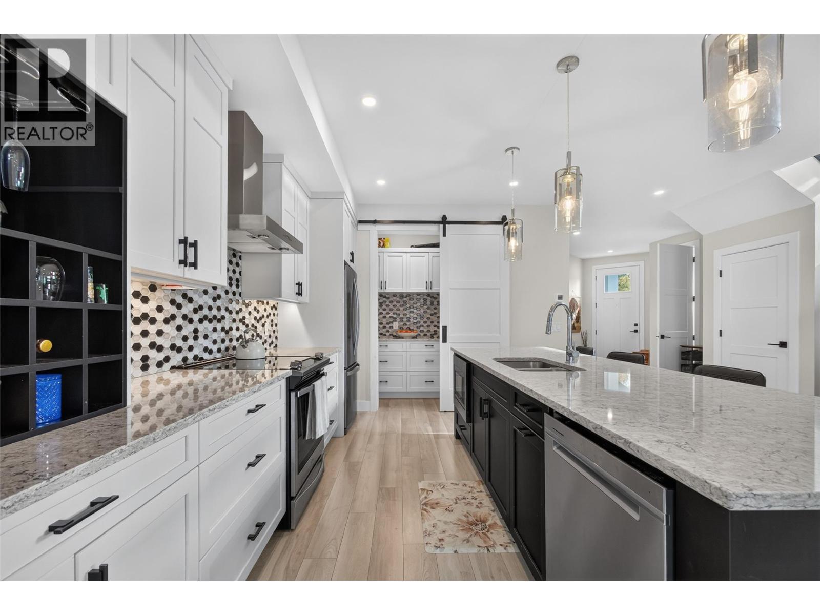 Thoughtfully designed kitchen with an oversized island, plenty of storage and a separate pantry tucked behind the sliding barn door. - 2400 Hawks Boulevard, West Kelowna, BC