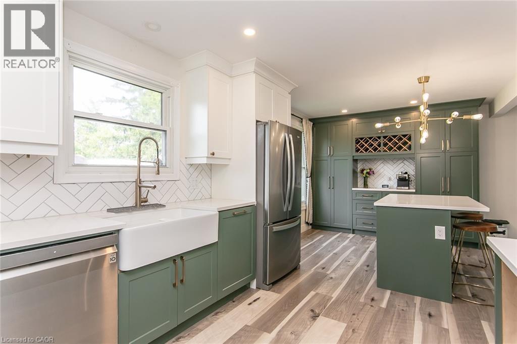 Updated kitchen featuring two-tone cabinetry, a farmhouse-style sink, a herringbone tile backsplash, and a central island with a countertop - 393 Huron Street, New Hamburg, ON