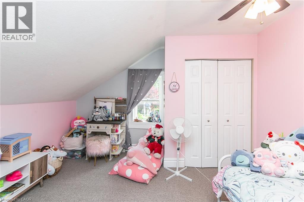 Sloped ceiling room featuring a window with curtain, built-in closet with bi-fold doors, and a ceiling fan - 393 Huron Street, New Hamburg, ON