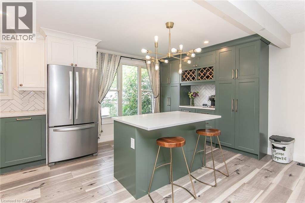 Kitchen featuring two-tone cabinetry, a central island with a solid surface countertop, wood-finish flooring, a herringbone tile backsplash, and a modern chandelier - 393 Huron Street, New Hamburg, ON