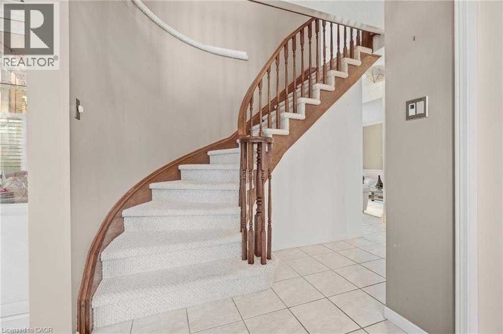 Curved staircase with wood-finish handrail and balusters, carpeted treads, and tiled flooring - 5 Michelle Drive, St. Catharines, ON