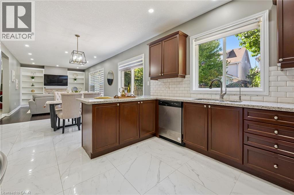 Gourmet kitchen featuring a stainless steel dishwasher, brown wood-finish cabinetry, granite-style countertops, white subway tile backsplash, and a large window above the sink - 154 Falconridge Drive, Kitchener, ON