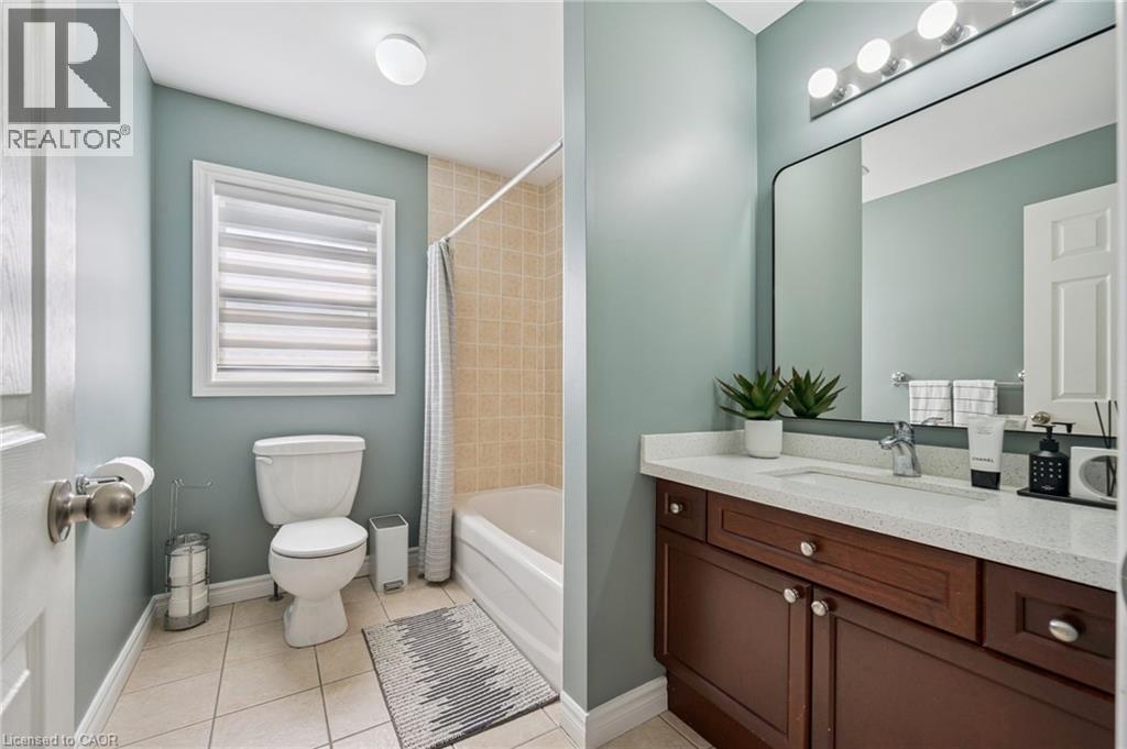 Bathroom featuring a vanity with a white countertop and wood-finish cabinetry, a rectangular mirror, and a bathtub with tile surround - 154 Falconridge Drive, Kitchener, ON