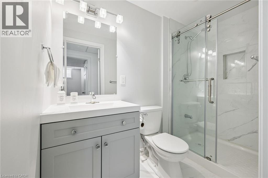 Vanity with a white countertop and gray cabinetry, mirrored medicine cabinet, and a glass-enclosed shower with a built-in niche - 154 Falconridge Drive, Kitchener, ON