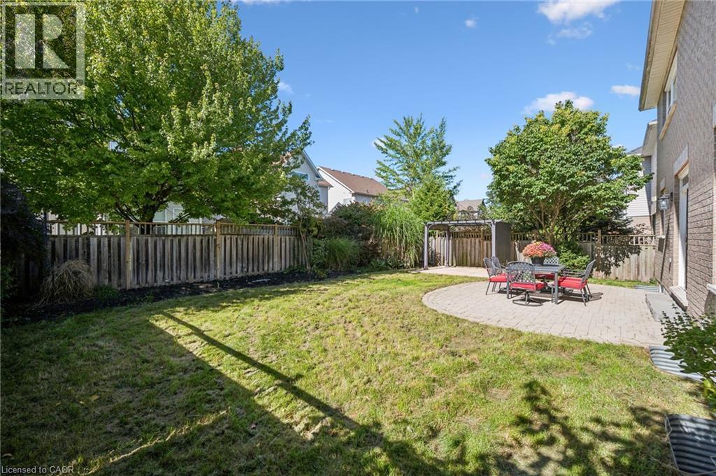 Expansive backyard featuring a circular paver patio, wood privacy fencing, mature trees, and a pergola structure - 154 Falconridge Drive, Kitchener, ON
