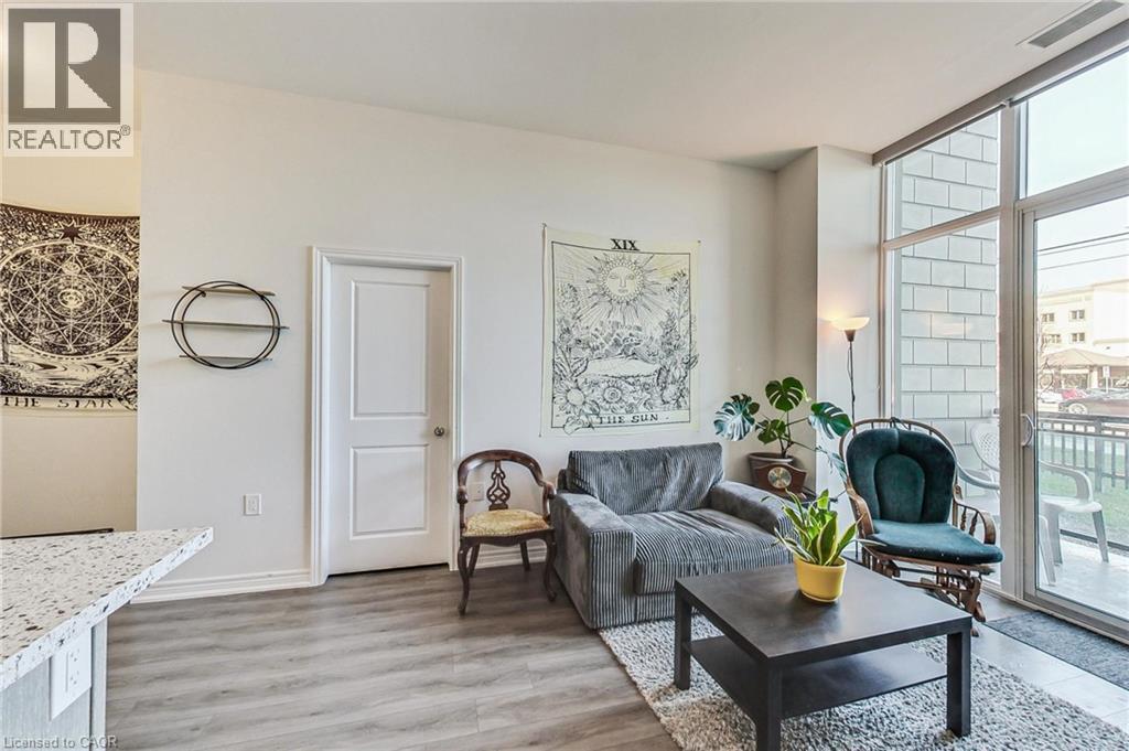 Light wood-finish flooring, white walls, and a built-in kitchen counter with a speckled surface - 2750 King Street E Unit# 103, Hamilton, ON