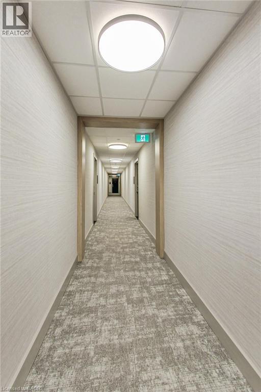 Corridor featuring patterned carpet, light wood-finish door frames, and flush-mount ceiling lighting - 2750 King Street E Unit# 103, Hamilton, ON