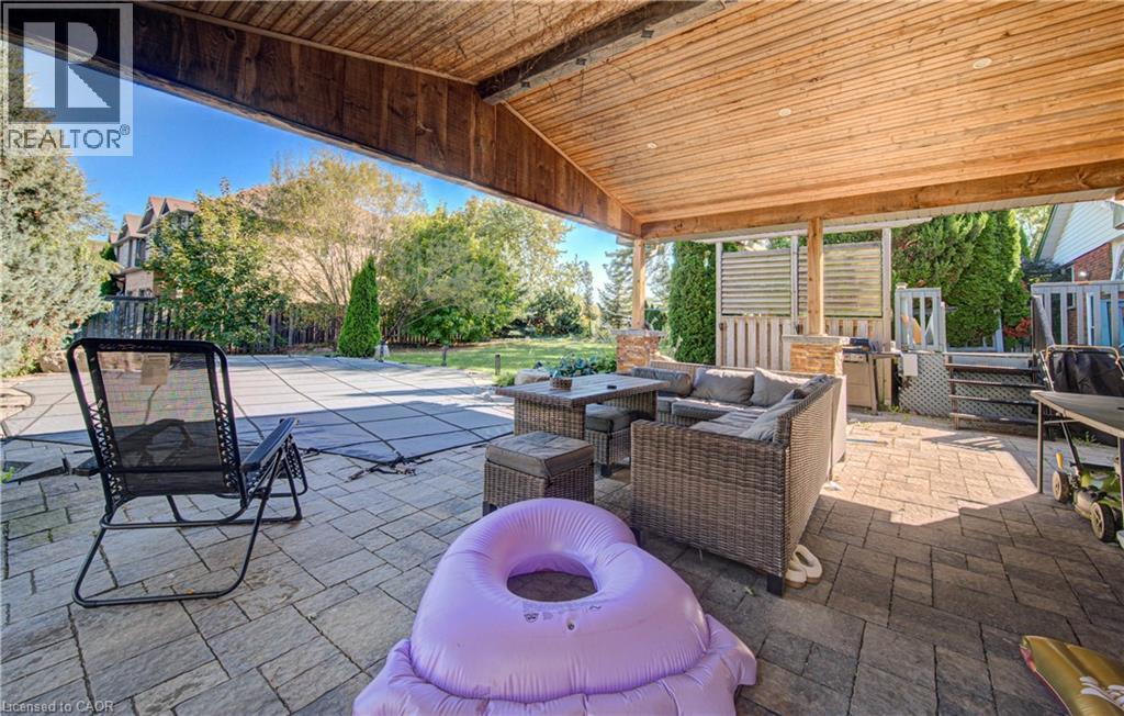 Expansive covered patio with wood-finish ceiling, paver stone hardscaping, stone-clad pillars, and a fully fenced yard - 3160 Binbrook Road, Binbrook, ON