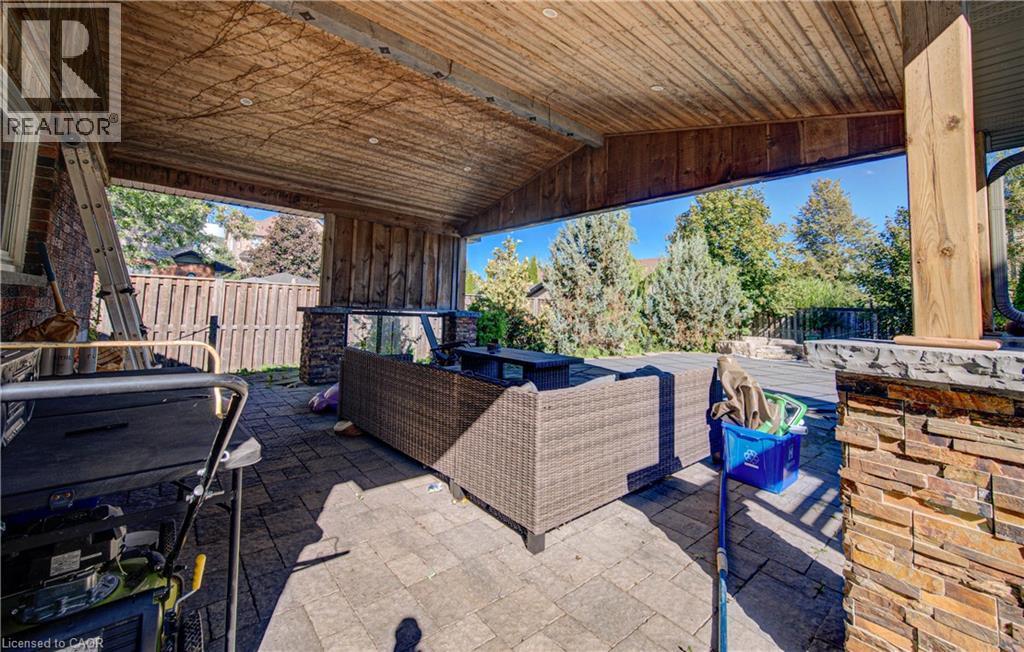 Covered outdoor patio featuring a wood-panel ceiling, stone-clad support pillars, and paver flooring - 3160 Binbrook Road, Binbrook, ON