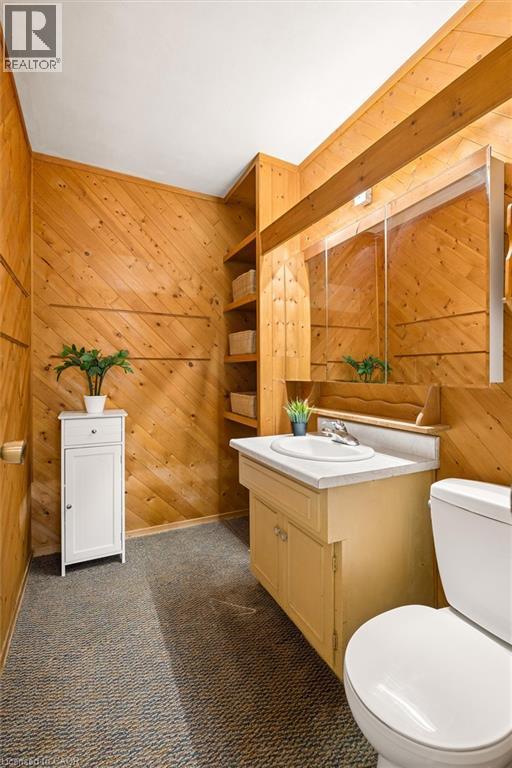 Wood-paneled walls, built-in shelving, white ceramic sink, light-toned vanity with cabinet storage, and a white toilet - 351 Craigleith Drive, Waterloo, ON