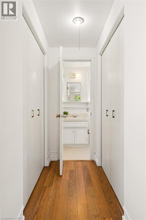 Hallway featuring wood-finish flooring, recessed ceiling light, and multiple storage closets with white doors and black hardware - 351 Craigleith Drive, Waterloo, ON