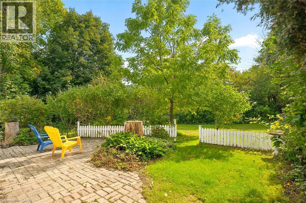 Expansive outdoor space featuring a paved patio, manicured lawn, picket fence, mature trees, and established plantings - 351 Craigleith Drive, Waterloo, ON