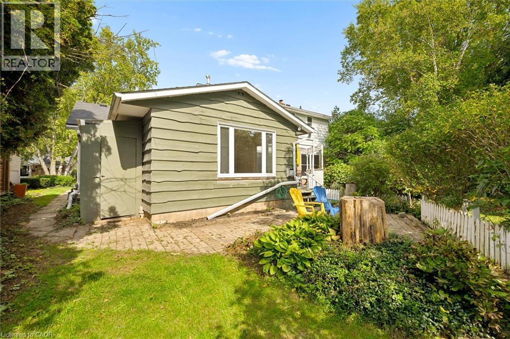 Exterior featuring green horizontal siding, a white-framed window, a brick paver patio, a white picket fence, and mature trees - 351 Craigleith Drive, Waterloo, ON
