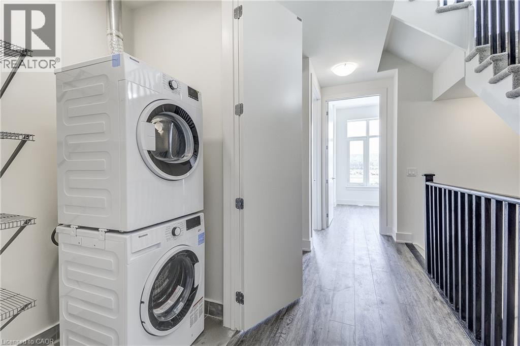 Stackable washer and dryer, wire shelving, dark wood-finish flooring, white walls, and a staircase with black railings - 58 Windward Drive, Grimsby, ON