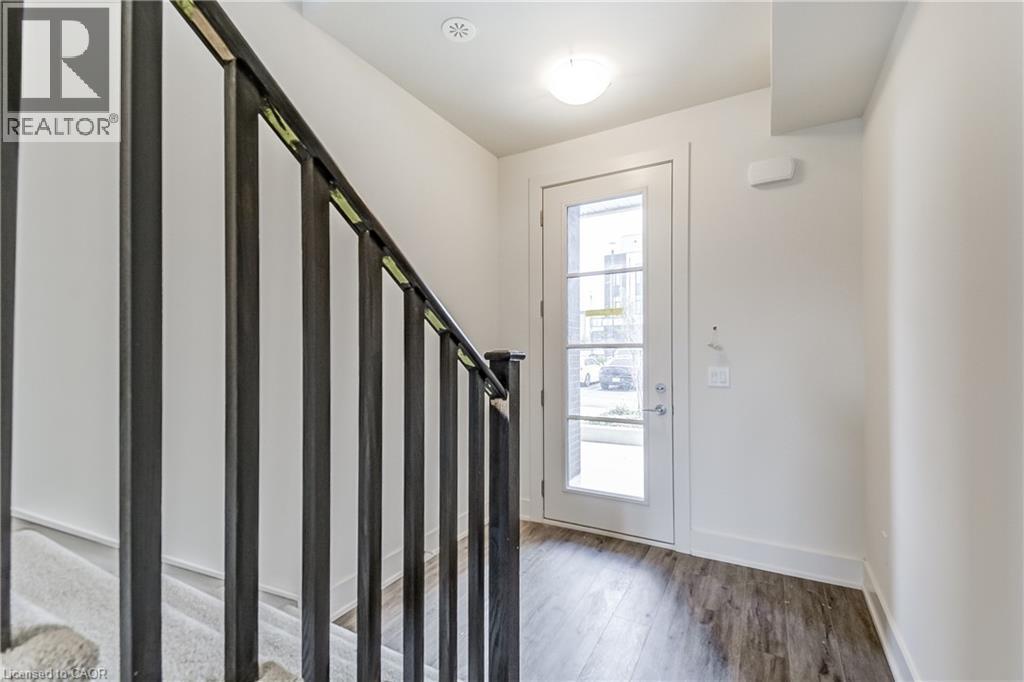 Staircase with dark metal balusters, wood-finish flooring, and a white paneled door with glass inserts - 58 Windward Drive, Grimsby, ON