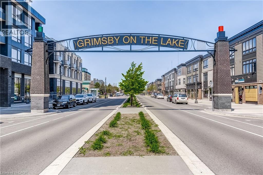 Street scene featuring a prominent archway, brick columns, and a central median with landscaping - 58 Windward Drive, Grimsby, ON
