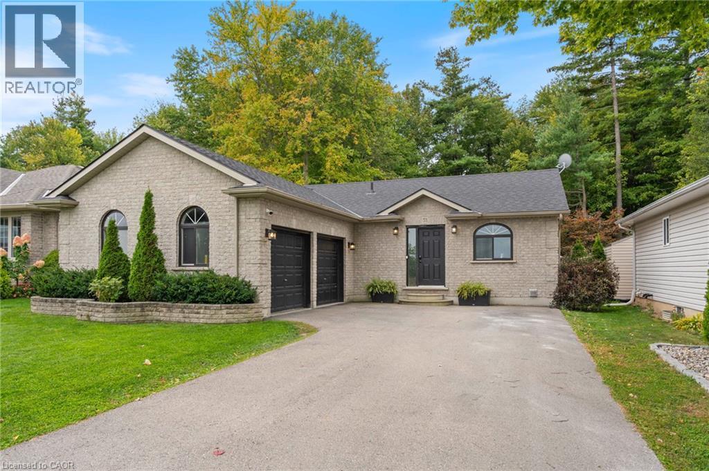 Light brick exterior with a dark shingled roof, featuring a two-car garage with dark doors, a paved driveway, and established landscaping - 53 Hawtrey Road, Delhi, ON