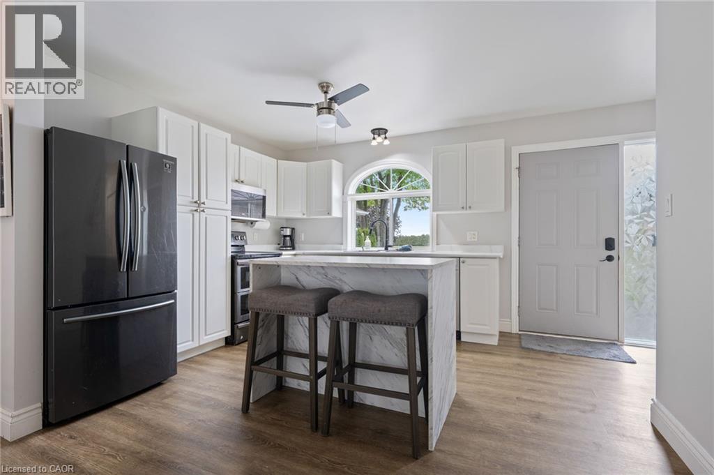 Bright kitchen with white cabinetry, wood-finish flooring, a central island featuring a waterfall countertop, and an arched window - 53 Hawtrey Road, Delhi, ON