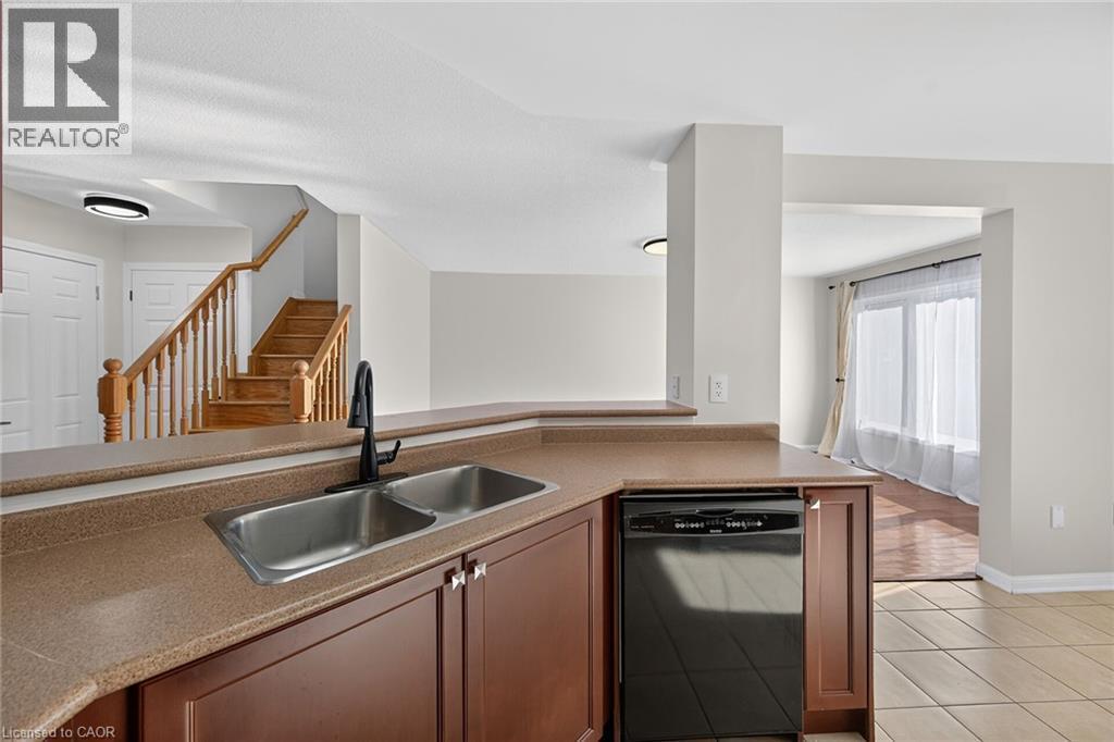 Kitchen area featuring a double basin stainless steel sink with a matte black faucet, dark wood-finish cabinetry, and a black built-in dishwasher - 103 Emick Drive, Ancaster, ON
