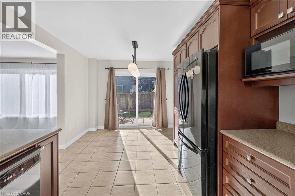 Kitchen featuring a black refrigerator, built-in microwave, wood-finish cabinetry, and solid surface countertops - 103 Emick Drive, Ancaster, ON