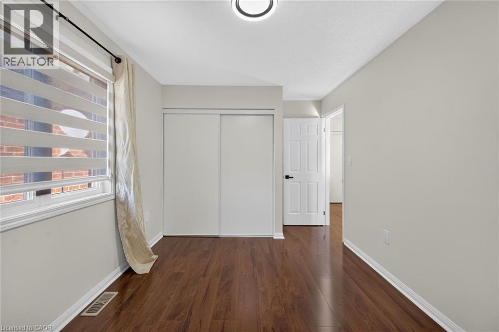 Wood-finish flooring with light gray walls, a window with roller shades, and a white sliding closet door - 103 Emick Drive, Ancaster, ON